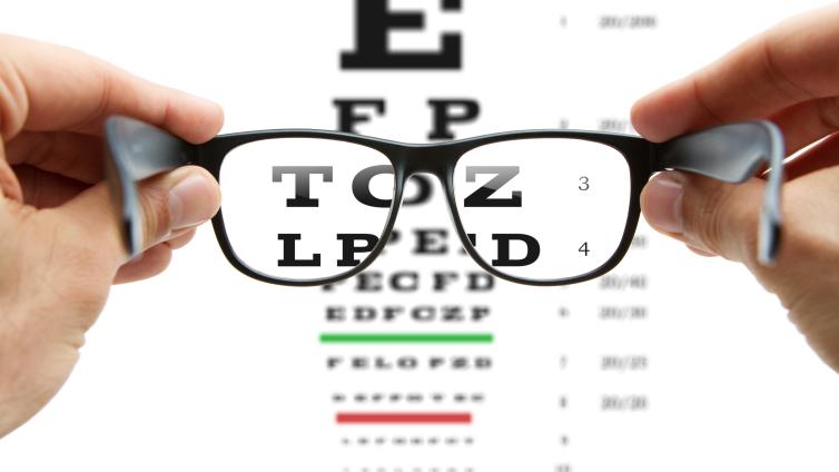 A pair of black glasses held in front of an eye examination chart.