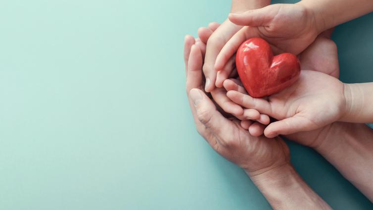 Hands overlapping and holding a heart figurine 