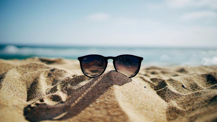 Sunglasses on sand with beach scene behind